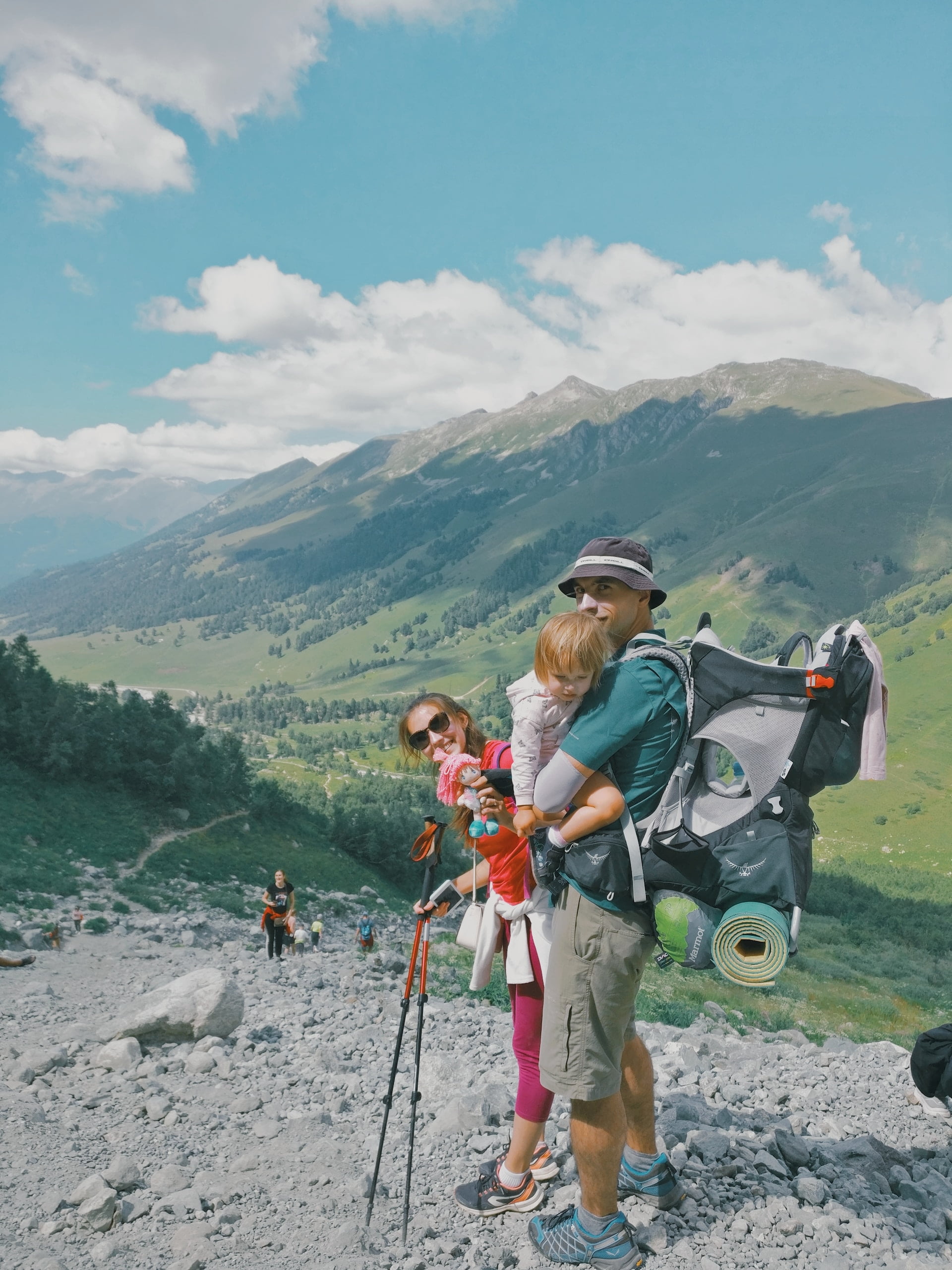 Happy young couple holding a baby while hiking in the middle of beautiful mountains.